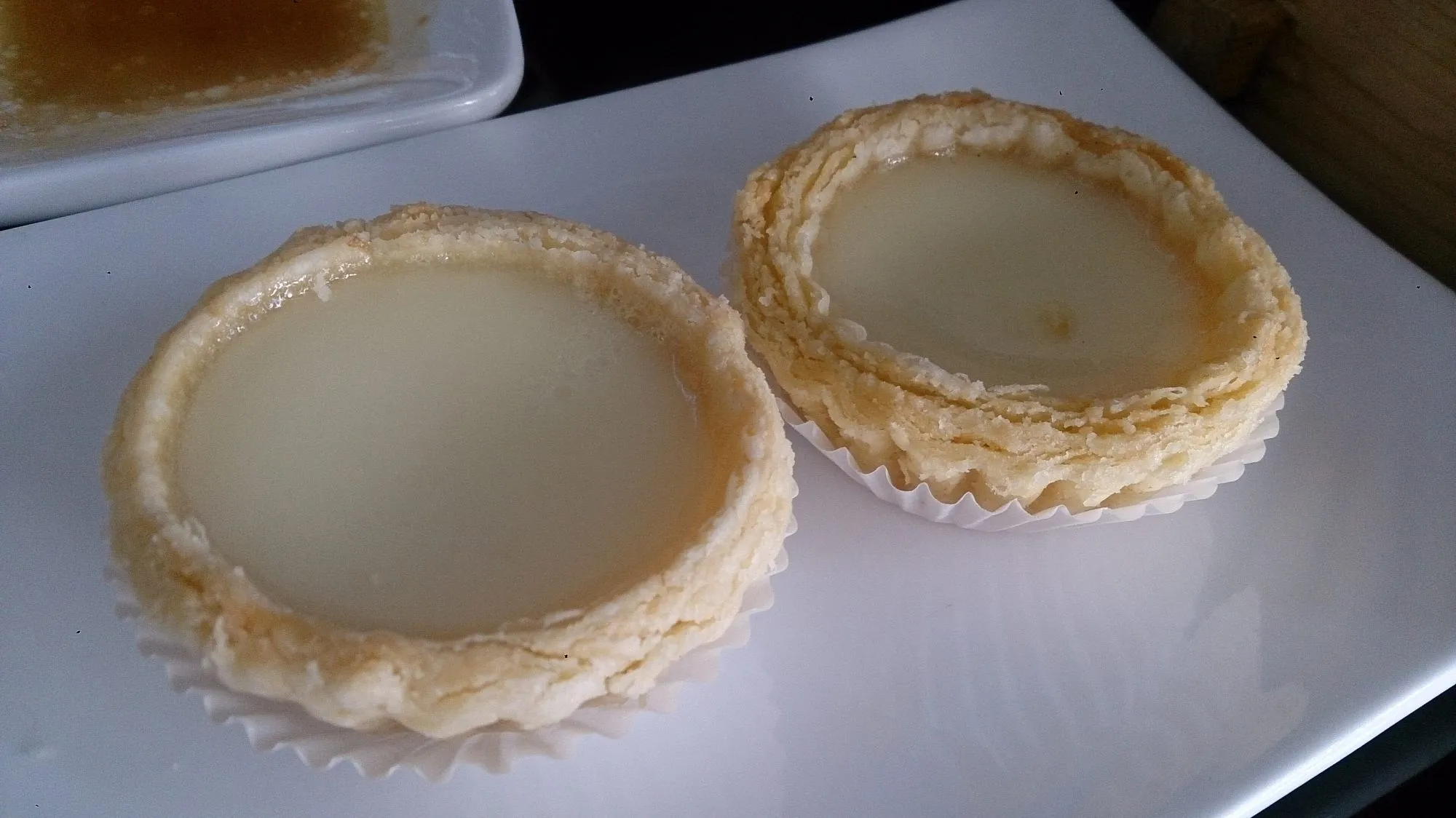 Two flaky Cantonese-style egg tarts with smooth yellow custard on a white plate