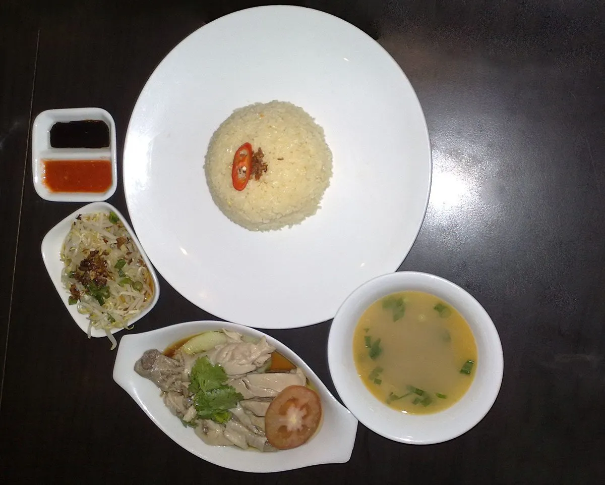 Set of poached chicken with blanched bean sprouts, rice, soup and sauces on a dark table