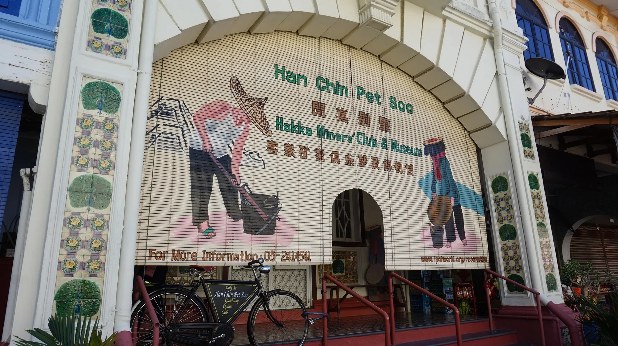 拱形店屋正面挂着画有矿工的竹帘，招牌写着 Han Chin Pet Soo Hakka Miners' Club and Museum