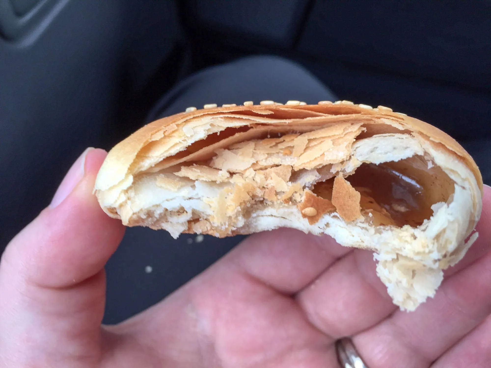 Hand holding a halved heong peng pastry showing a flaky crust and sticky maltose filling