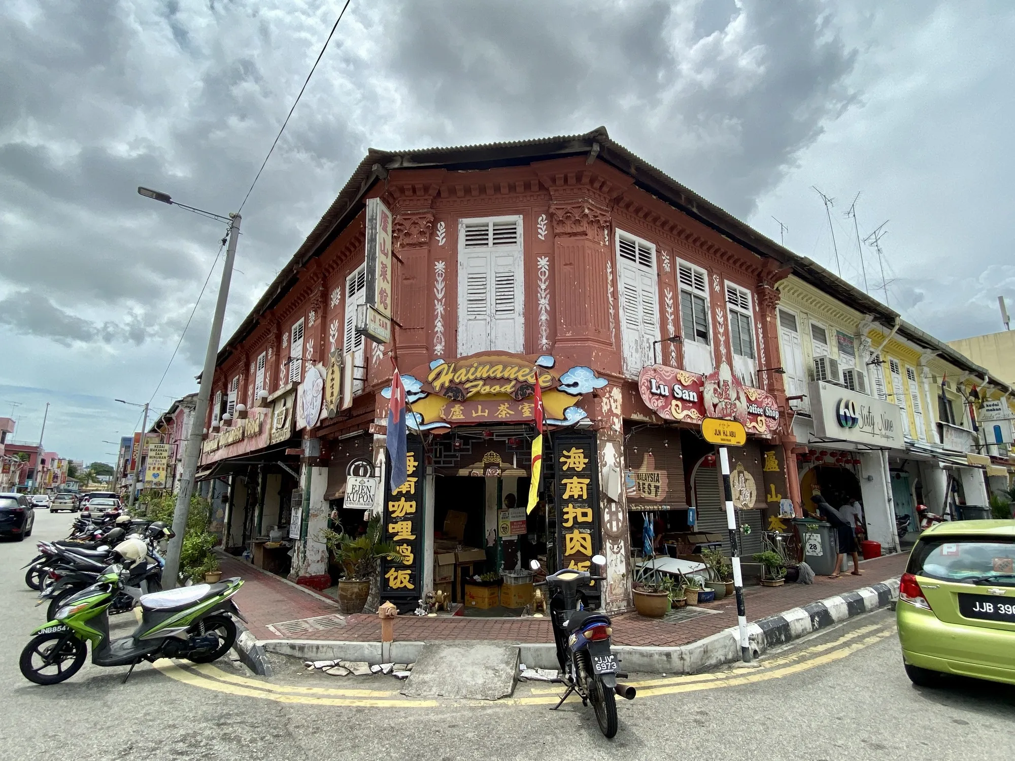 Kedai kopi di rumah kedai warisan dua tingkat di simpang, dengan bahagian hadapan terbuka dan motosikal diletakkan