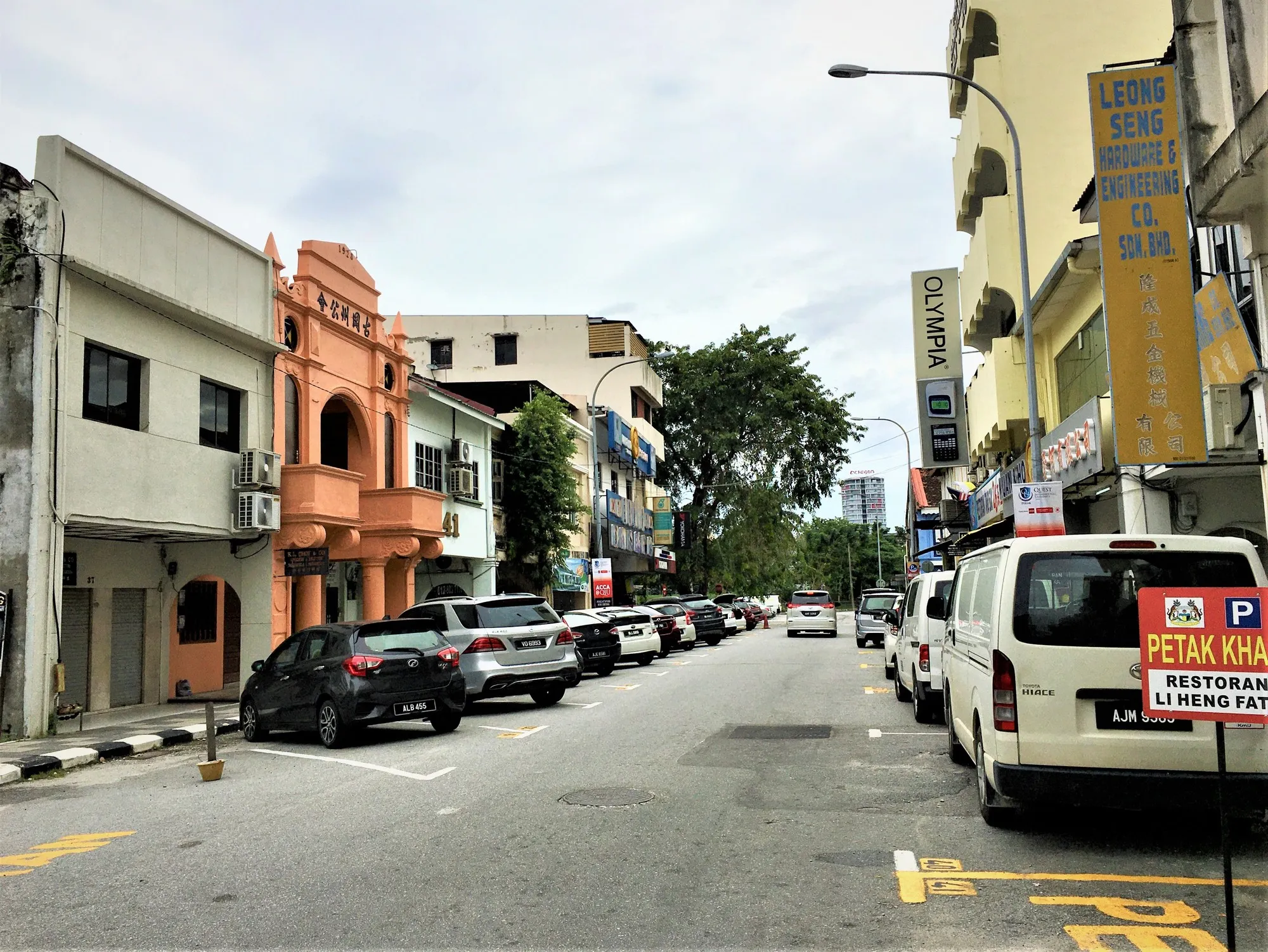 Street of mixed old shophouses with parked cars and a salmon-pink 1920s clan house facade on Jalan Panglima, Ipoh