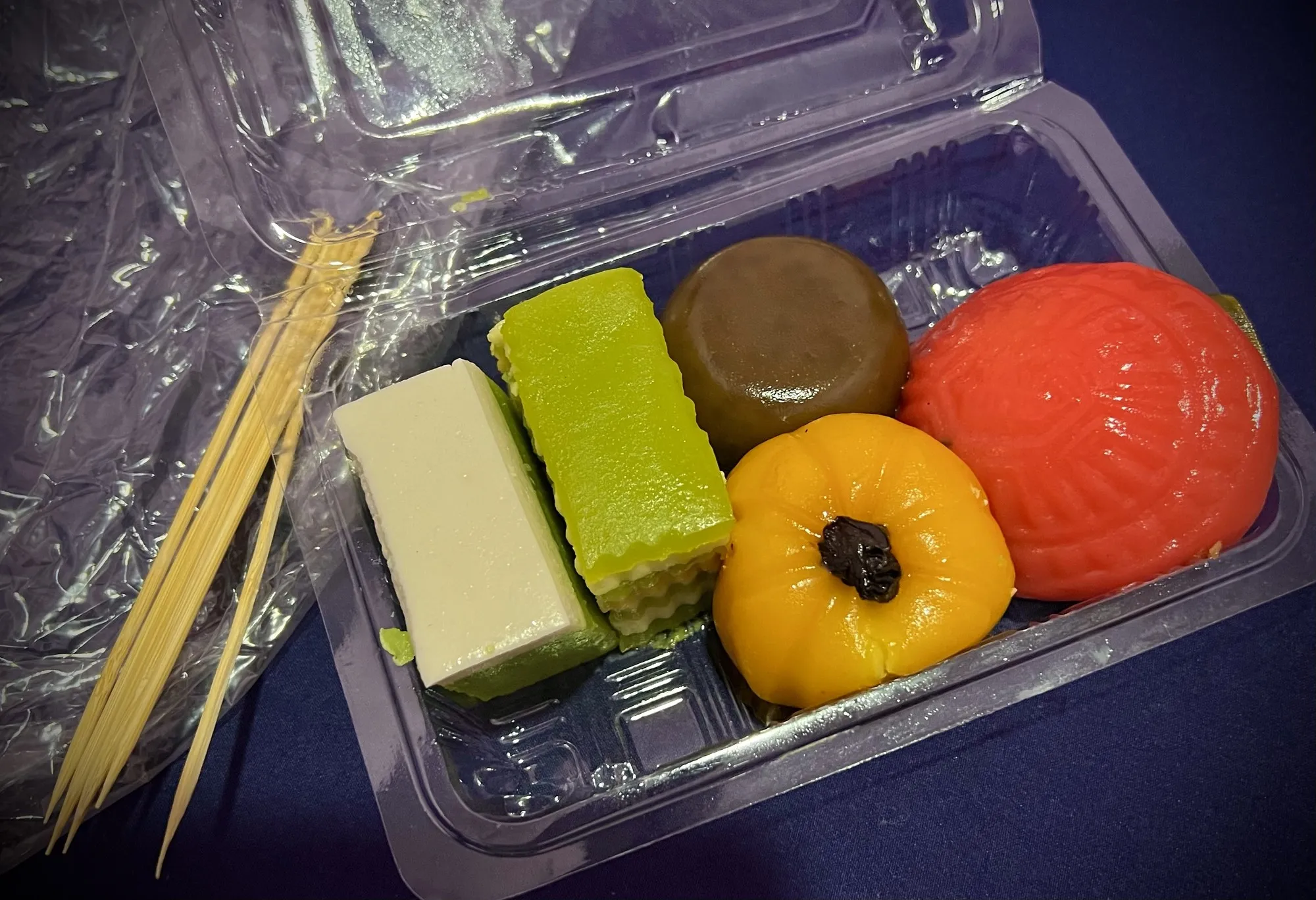 Sekotak kuih Nyonya berwarna-warni: kuih lapis hijau dan kuning, kuih bulat perang dan ang ku kuih merah jingga