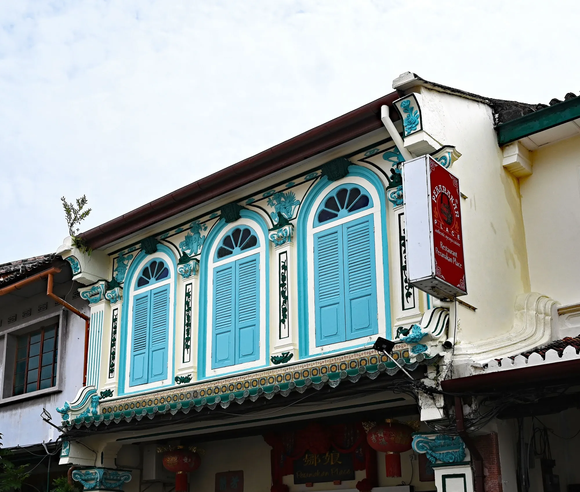 Rumah kedai berhias gaya Peranakan di Melaka dengan tingkap berlengkung berbidai biru, jubin hijau dan acuan plaster