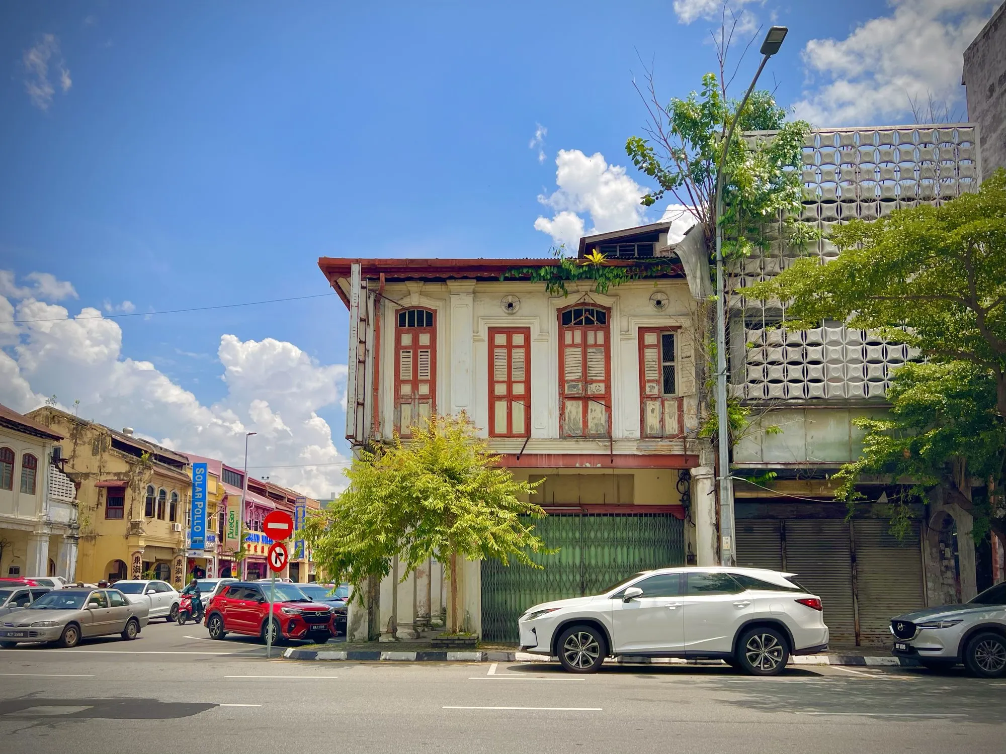 Weathered white shophouse corner in Ipoh with arched red-framed shutters and a green metal gate